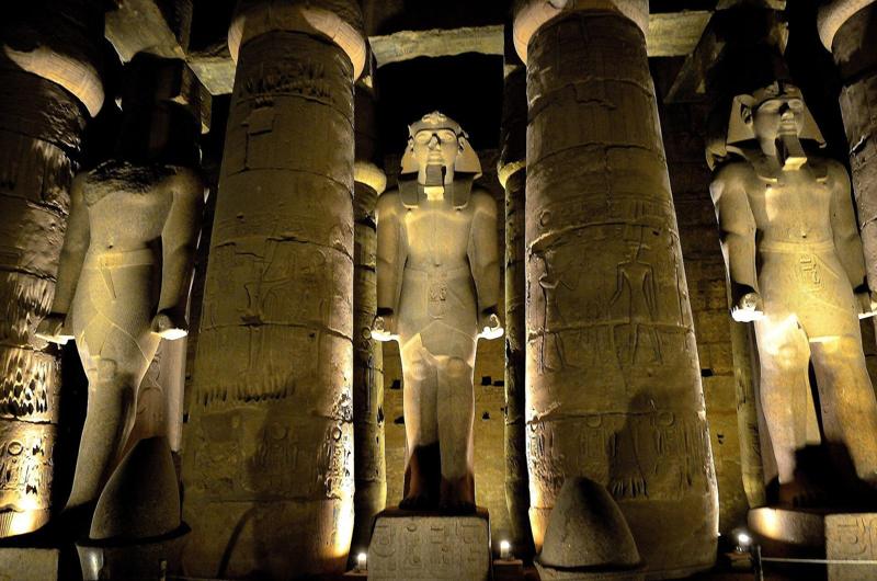Floodlit columns and pharaoh statues inside a temple at night, Luxor